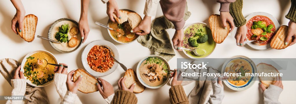 People eating various Autumn and Winter creamy vegan soups together People eating Autumn and Winter creamy vegan soups. Flat-lay of peoples hands, soup plates and bread slices over plain white table background, top view. Fall and Winter food menu, vegetarian food Soup Stock Photo