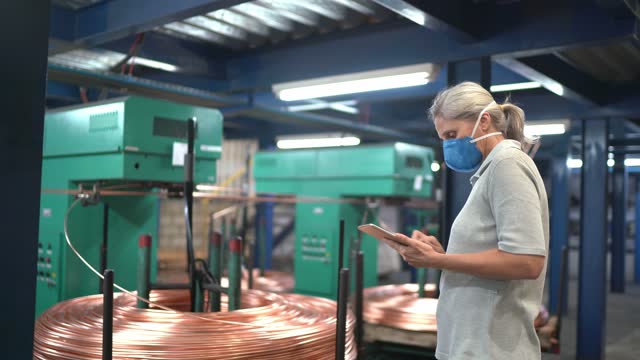 Mature woman wearing face mask and using digital tablet working in a metal industry