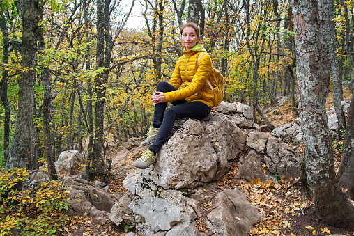 Relaxed woman siting on a stone in autumn mountain forest