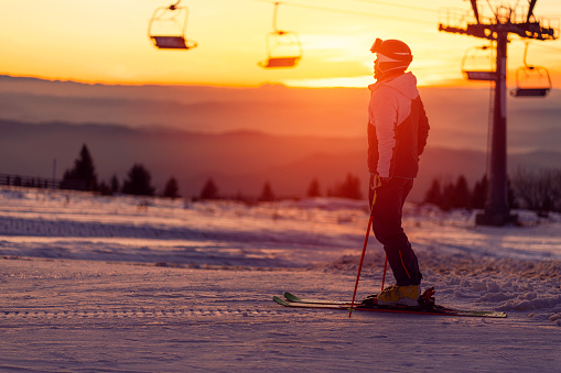 Side view of a young male skier standing on the skis and watching a sunset.