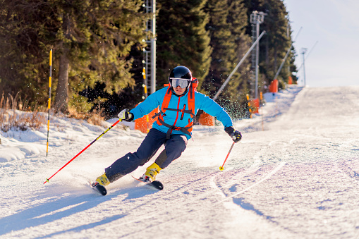 Male athlete skiing down the snowy ski slope on a sunny winter day.