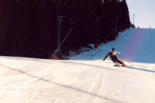Male athlete skiing down the snowy ski slope on a sunny winter day.