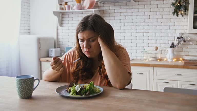 Boring diet. Depressed overweight woman eating untasty healthy salad at kitchen