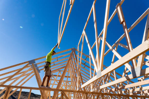 ein framer, der auf den skelton-wänden eines neuen eigenheimbaus steht und den kranführer dazu führt, einen weiteren truss zu setzen - lowering sky stock-fotos und bilder