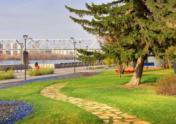 Mikhailovskaya embankment of the Ob river Winding pedestrian path on a green lawn, railway bridge in the distance western siberia stock pictures, royalty-free photos & images
