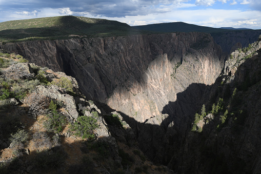 During mid-summer afternoon, the Black Canyon of the Gunnison shows unusual light effect of a “bear” walking down the slopes. Black Canyon displays some of the steepest cliffs and oldest rocks in North America. The Gunnison River, with two million years of work, has sculpted this vertical wilderness in hard, dark-colored Precambrian gneiss, which had been later crosscut with light pegmatite dikes.