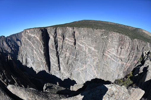 Wide angle view of the famous Painted Wall of Black Canyon of the Gunnison in Colorado. This Canyon displays some of the steepest cliffs and oldest rocks in North America. The Gunnison River (in a shadow of the  bottom), with two million years of erosion work, has sculpted this vertical wilderness in hard, dark-colored Precambrian gneiss, which had been later crosscut with light pegmatite dikes.