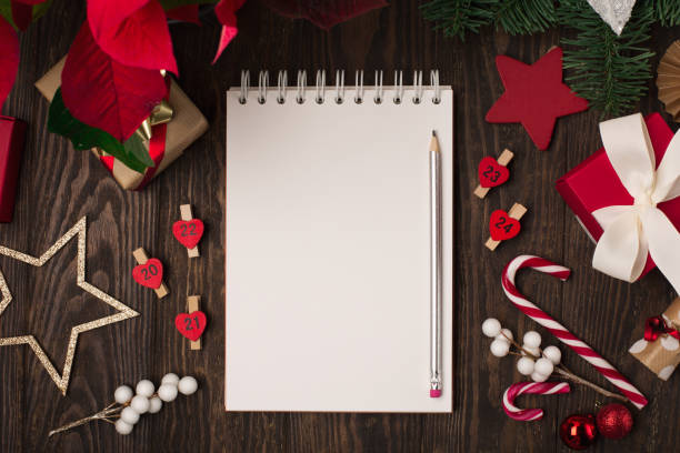 istock Empty white notebook, red flower poinsettia, Christmas decorations, gift boxes and candy canes on dark wooden background. 1286778545