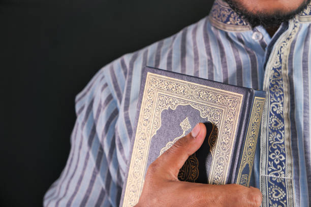 istock Muslim man hand holding Quran isolated on black 1286785904