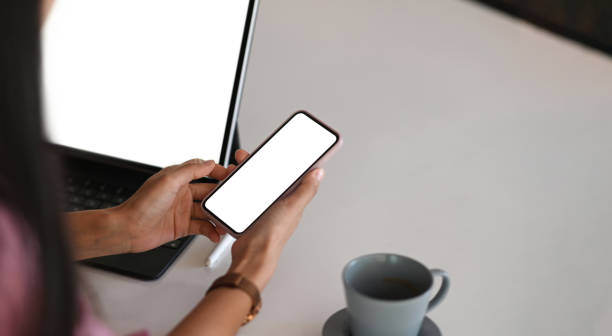 istock Cropped shot of young woman is sitting in front of computer tablet while using mobile phone. For graphic display montage. 1286801892