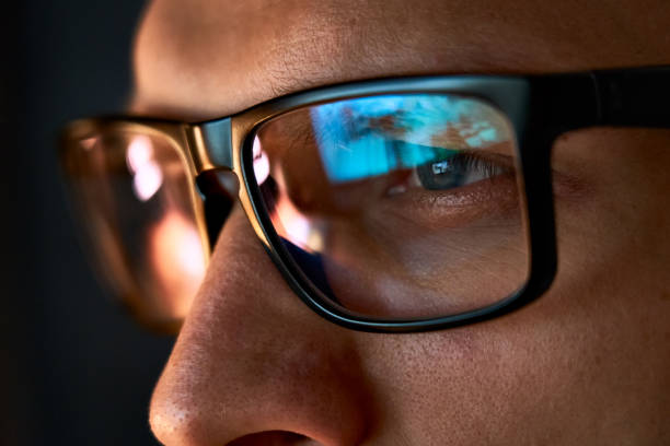 close up view of focused businessman wears computer glasses for reducing eye strain blurred vision looking at pc screen with computer reflection using internet, reading, watching, working online late. - computer thinking men people imagens e fotografias de stock