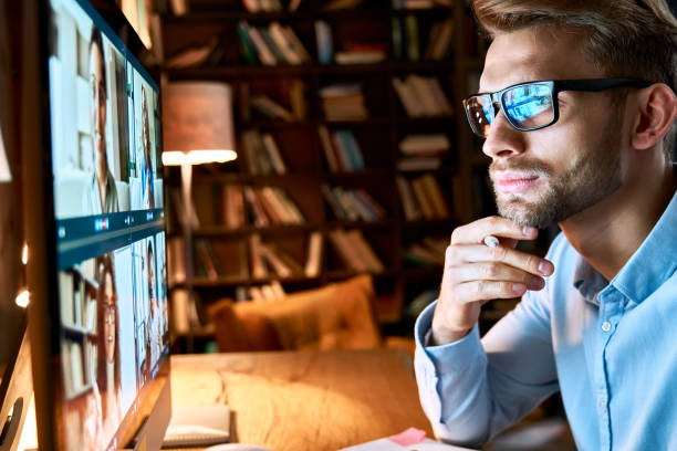 Serious young businessman wearing glasses looking at pc computer screen working online by video conference call having remote social distance online team virtual chat meeting concept, close up view.