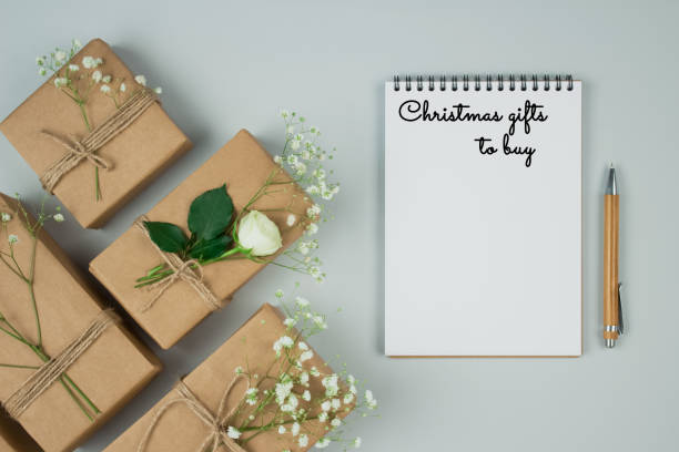 istock Christmas flat lay minimal composition with wooden pen, notebook and gift or presents boxes, wraped with kraft paper on grey background with copyspace. Holiday shopping list concept 1286804849