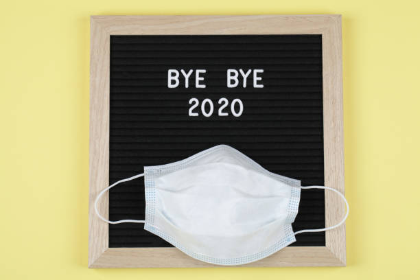 black letter board with text BYE BYE 2020 with mask on yellow background. . Top view. flat lay New Year Christmas minimal background