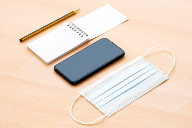 istock A face mask, a blank spiral notepad with a pen and a smartphone are arranged on a wooden table. 1286805698