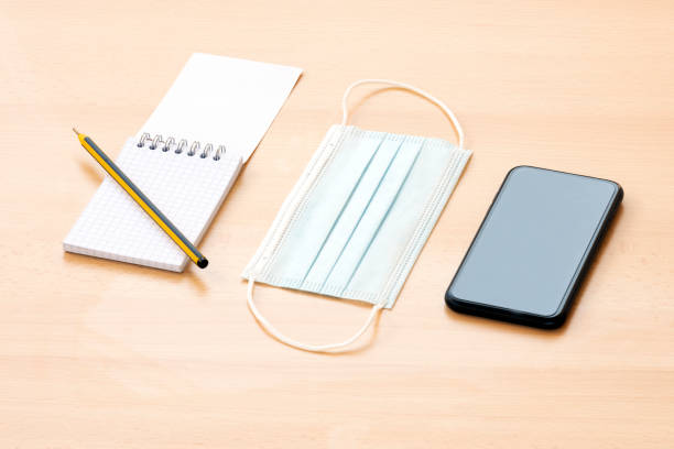 istock A face mask, a blank spiral notepad with a pen and a smartphone are arranged on a wooden table. 1286805708