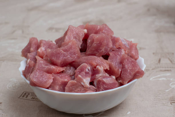 Sliced raw meat in a white bowl on a light table. View from above
