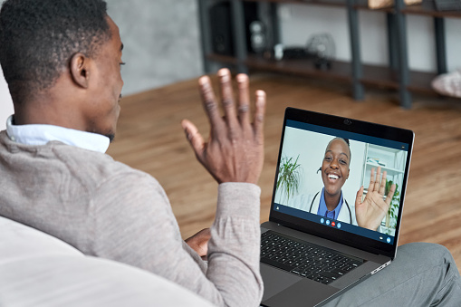 Paciente negro macho hablando en videoconferencia a la doctora africana. Terapeuta virtual consultando al joven durante la cita en línea en el ordenador portátil en casa. Chat de telemedicina, reunión de telesalud photo