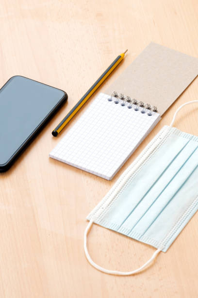 istock A face mask, a blank spiral notepad with a pen and a smartphone are arranged on a wooden table. 1286811809