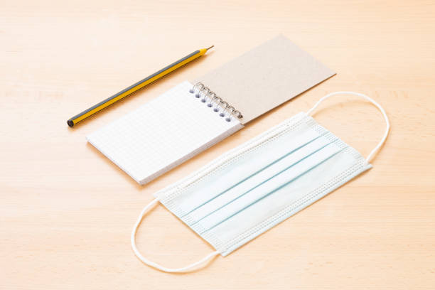 istock A face mask and a blank spiral notepad with a pen are arranged on a wooden table. 1286812759
