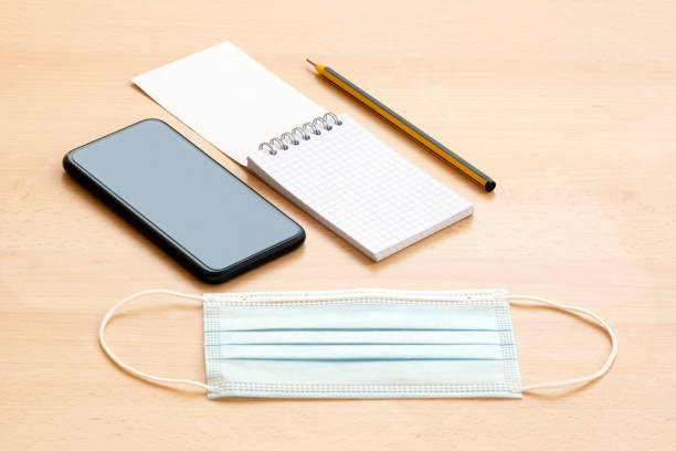 istock A face mask, a blank spiral notepad with a pen and a smartphone are arranged on a wooden table. 1286812783