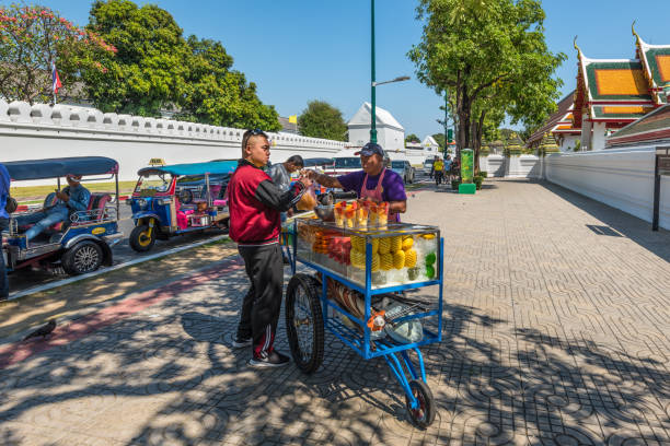A street vendor with his fruit cart in Bangkok, Thailand Bangkok, Thailand - December 7, 2019: A fruit cart vendor is selling fruits for his customer on side walk in Bangkok, Thailand. fruit cart vendor stock pictures, royalty-free photos & images