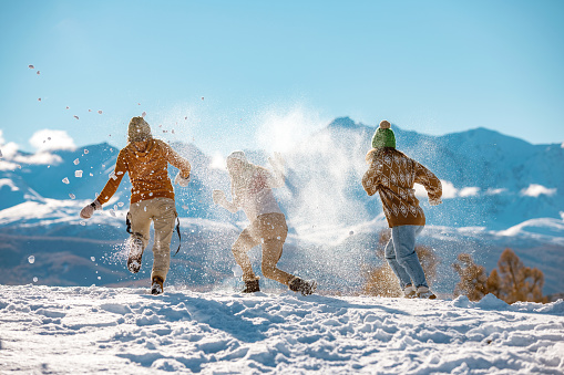 Three young happy girls friends are having fun in snow fight in mountains. First snow and winter vacations concept