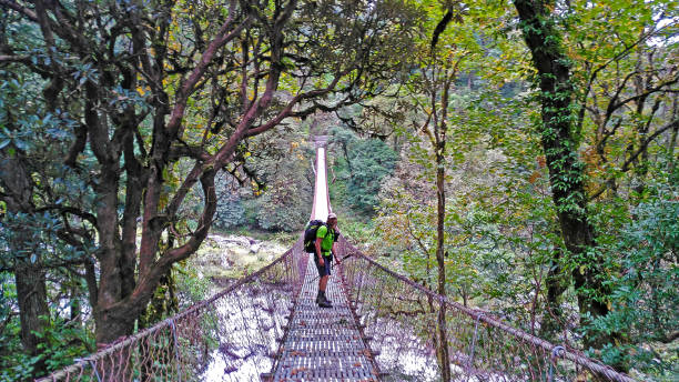 istock Backpacking hiker young man crossing a suspension bridge over a nepal river covered whit forest in the Annapurnas Round Trek Circuit. 1286818584