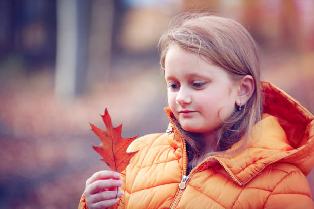 Thoughtful girl in the autumn forest watching an oak leaf