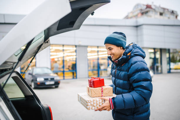 istock Smiling young man holding presents loading his car trunk. Consumerism / shopping concept. Special occasion / holiday shopping concept. 1286825710