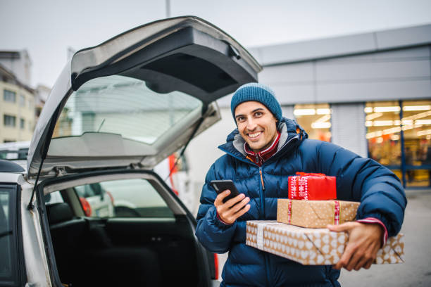 istock Smiling young man holding presents loading his car trunk. Consumerism / shopping concept. Special occasion / holiday shopping concept. 1286825712