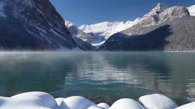 Lake Louise in early winter sunny day morning. Mist floating on turquoise color water surface
