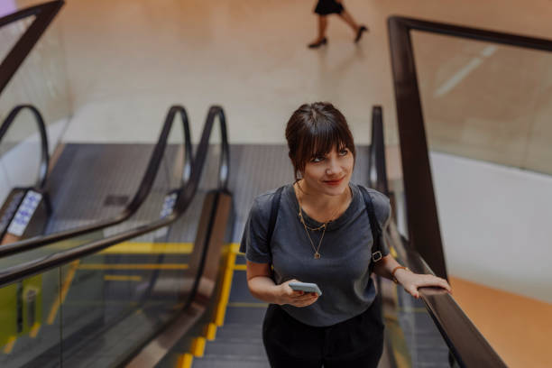 istock Staying Connected:  Beautiful Woman Holding her Mobile Phone While Riding an Escalator 1286826065