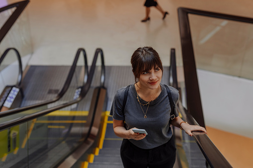 Happy woman texting on an escalator.