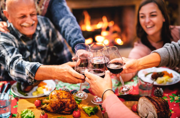 people toasting red wine glass having fun at christmas supper reunion - holiday celebration concept with happy family sharing winter time together at home fireplace - warm filter with focus on hands - celebrating friends winter imagens e fotografias de stock