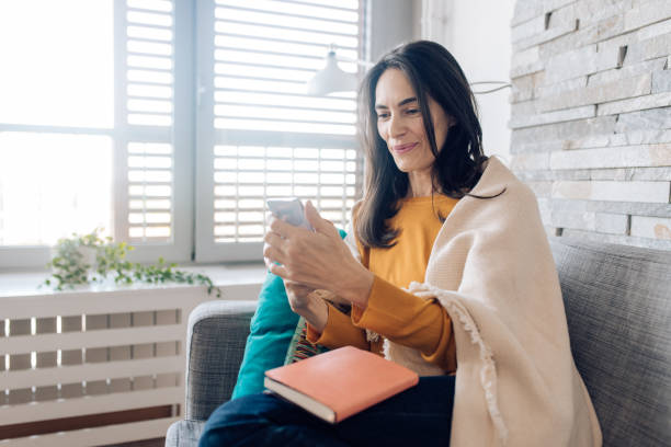 istock Mature woman relaxing on the sofa and using her smartphone after reading 1286835085