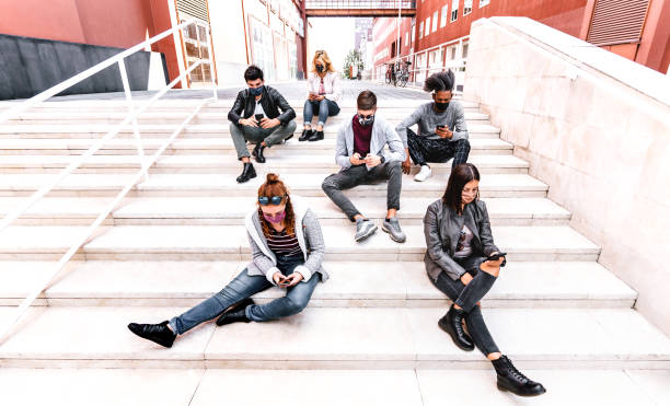 istock Urban milenial people using smart phones covered by face mask on Covid second wave - Worried guys and girls watching video on smartphone - College students sitting at university break - Bright filter 1286835854