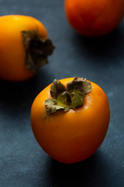 istock Whole sweet orange persimmon fruits isolated on dark background. Copy space. 1286836615