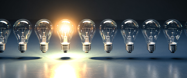 A row of lightbulbs with one brigthly lit - concept for having an idea, innovation, standing out. Web banner size