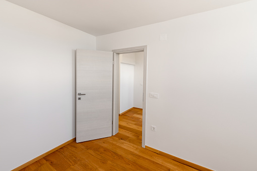 Empty apartment with white walls and wooden floor, ready to move in. Doors open on hallway