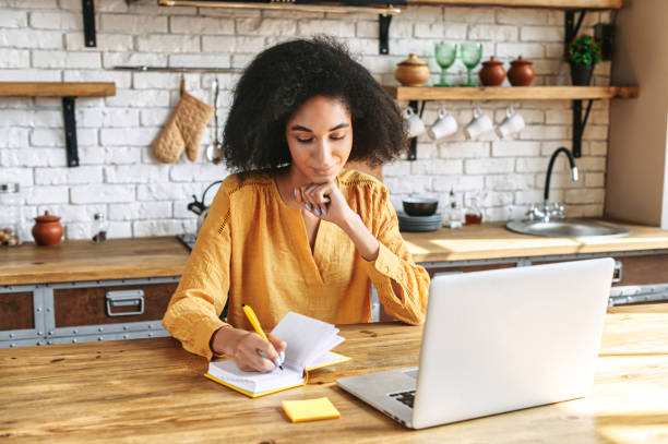 istock Beautiful afro girl writes in notebook from laptop 1286842811
