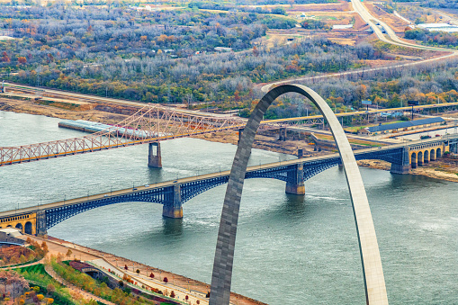 An aerial view of the mighty Mississippi River spanned by two bridges into St. Louis, Missouri with the top of the Gateway Arch in the foreground.
