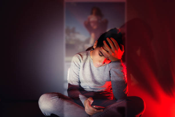 The Social Media Overuse A 13-year-old girl is using her smartphone in the dark room. The content she is browsing projects in front of her. cyberbullying stock pictures, royalty-free photos & images