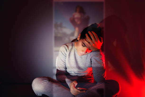 The Social Media Overuse A 13-year-old girl is using her smartphone in the dark room. The content she is browsing projects in front of her. child sadness stock pictures, royalty-free photos & images