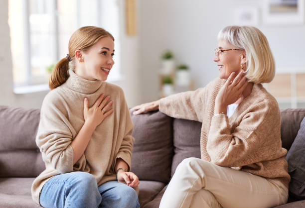 Mother and daughter speaking on couch Young woman smiling and talking with senior mother while sitting on comfortable sofa at home together mother in law stock pictures, royalty-free photos & images