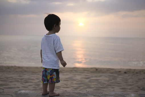 Portrait of a little boy standing looking at the vast sea. A picture of a little boy standing to look at the vast sea and the sunset. Copy space for caption on right side.