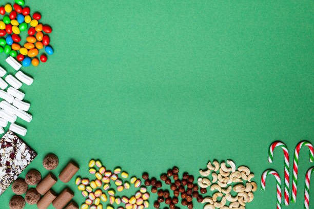 tło żywnościowe. różne kolorowe cukierki i nakrętki na zielonym tle z przestrzenią kopiowania. czekolada, lizaki, pianki, orzechy i inne słodycze. - marshmallow roasted stick candy zdjęcia i obrazy z banku zdjęć