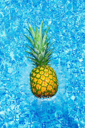 Pineapple falling into water with splashes in swim pool at sunny day. Tropical summer vacation concept card.