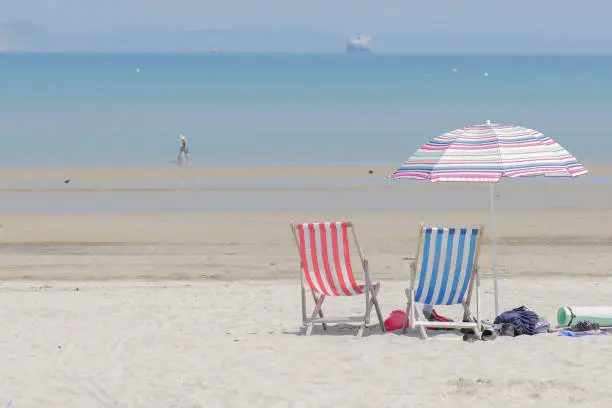 Beach in Engeland Weymouth with chairs and a Beach umbrella, birds, tanker boat, and two persons in the sea