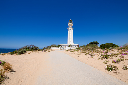 lonely dirty road with sand to the lighthouse of Cape Trafalgar, in Canos Meca village (Barbate, Cadiz, Andalusia, Spain), blue sky